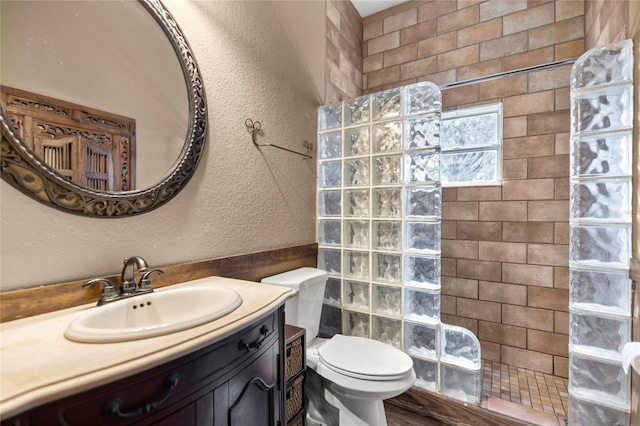 full bathroom with a walk in shower, a textured wall, toilet, and vanity