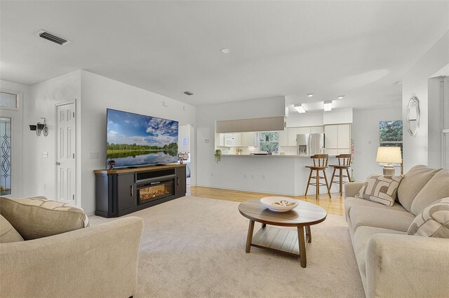 living room with a glass covered fireplace, light wood-style floors, and recessed lighting
