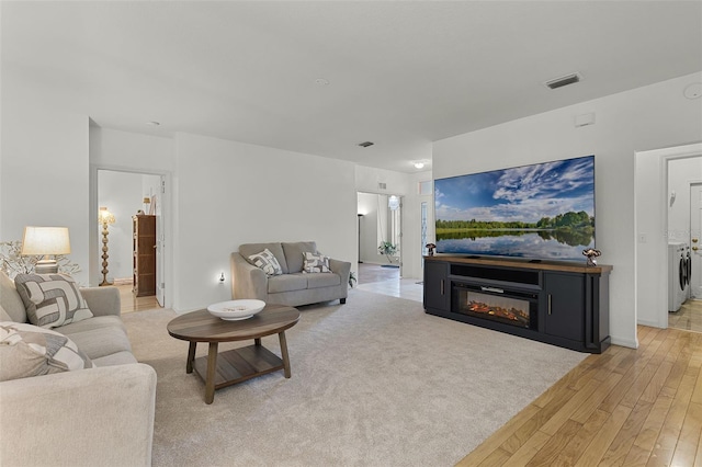 living room with light wood-type flooring, washing machine and clothes dryer, and a glass covered fireplace