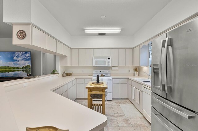 kitchen featuring white appliances, a sink, light countertops, and a peninsula