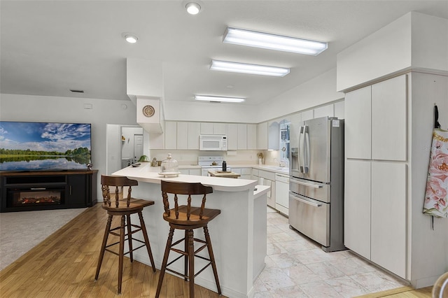 kitchen with white appliances, a kitchen breakfast bar, a peninsula, a glass covered fireplace, and white cabinets