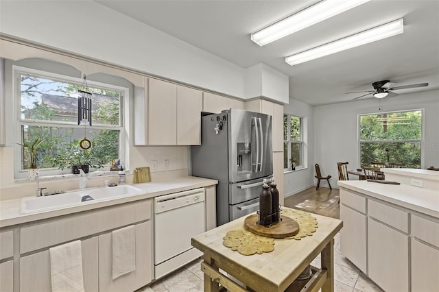 kitchen featuring white dishwasher, a sink, stainless steel fridge, light countertops, and backsplash