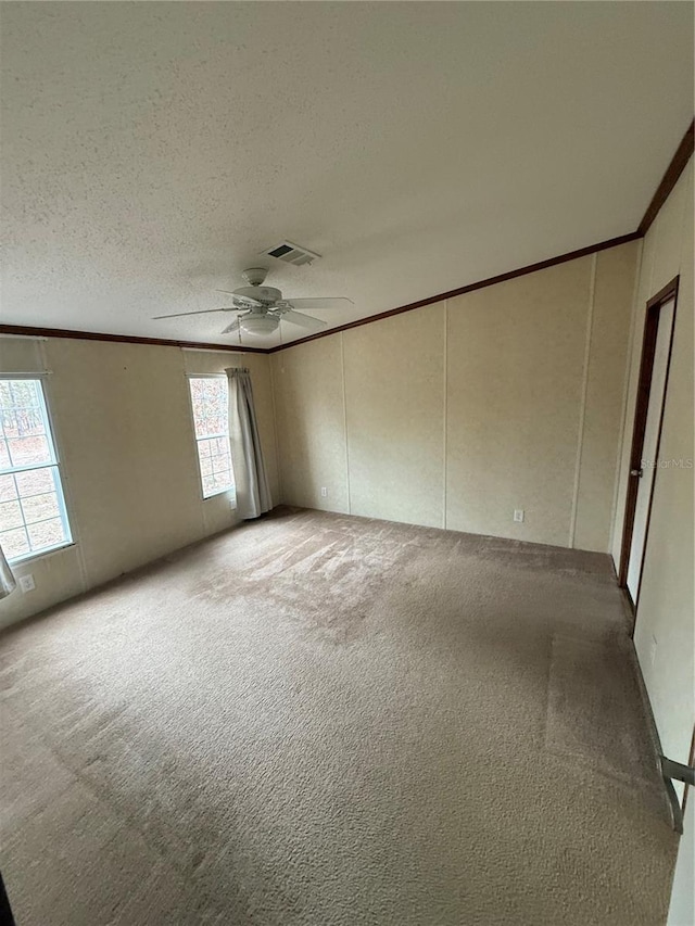 unfurnished room with ornamental molding, carpet, a ceiling fan, and visible vents