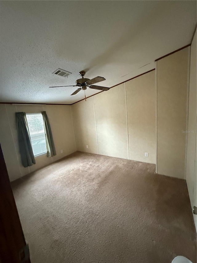 carpeted empty room with a decorative wall, a ceiling fan, and visible vents