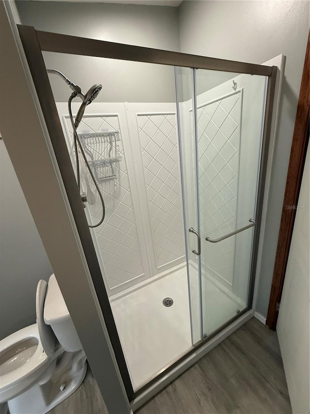 bathroom with toilet, a shower stall, and wood finished floors