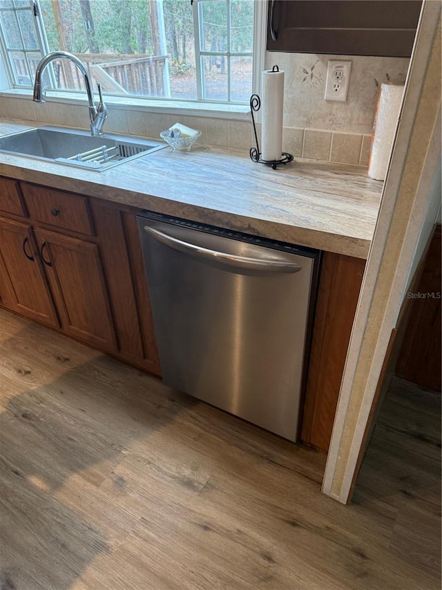 kitchen featuring stainless steel dishwasher, brown cabinetry, light wood-type flooring, light countertops, and a sink