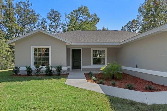 view of front facade with a shingled roof, stucco siding, and a front lawn