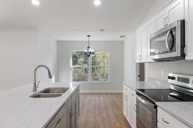 kitchen featuring appliances with stainless steel finishes, a sink, light wood-style floors, decorative light fixtures, and visible vents