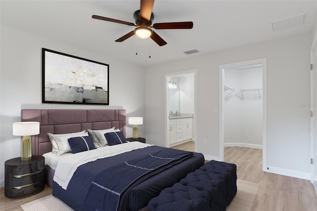 bedroom with a walk in closet, visible vents, a closet, ensuite bathroom, and light wood-style flooring