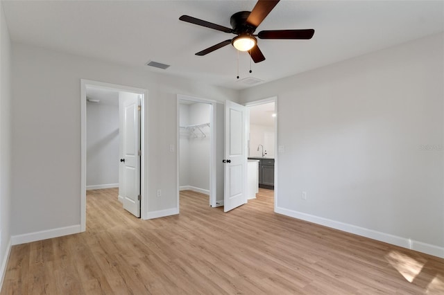 unfurnished bedroom with a spacious closet, baseboards, light wood finished floors, and visible vents