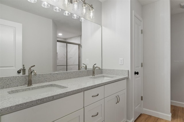 full bath featuring wood finished floors, double vanity, a sink, and a stall shower