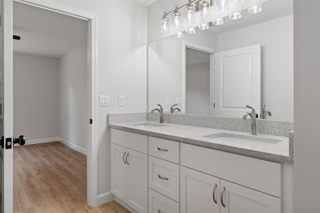 full bathroom with double vanity, baseboards, a sink, and wood finished floors