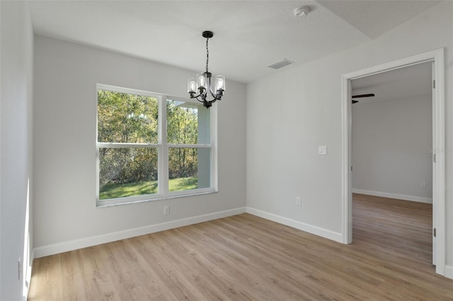 empty room featuring visible vents, a chandelier, a wealth of natural light, and light wood finished floors