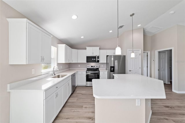 kitchen with appliances with stainless steel finishes, a sink, lofted ceiling, a center island, and light countertops