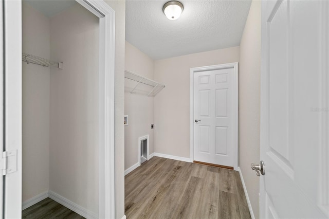 washroom featuring light wood-type flooring, baseboards, hookup for an electric dryer, and a textured ceiling