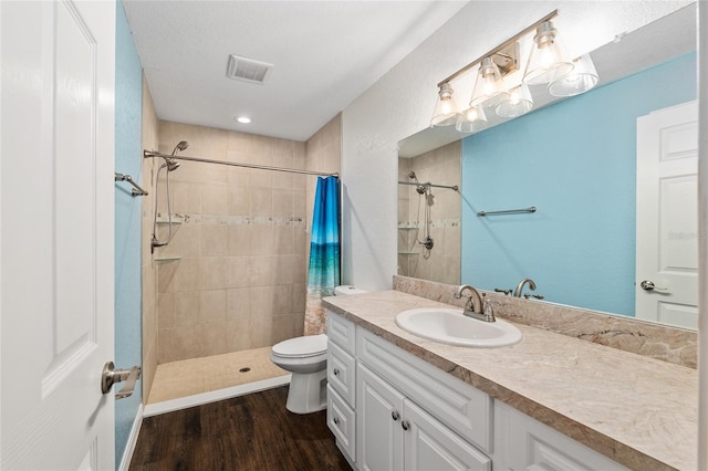 full bath with wood finished floors, vanity, tiled shower, and visible vents