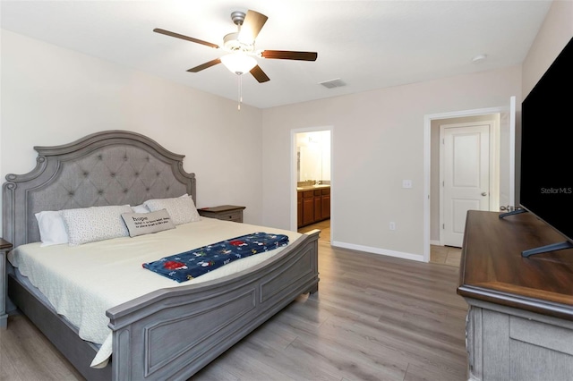 bedroom featuring a ceiling fan, visible vents, baseboards, light wood finished floors, and ensuite bath