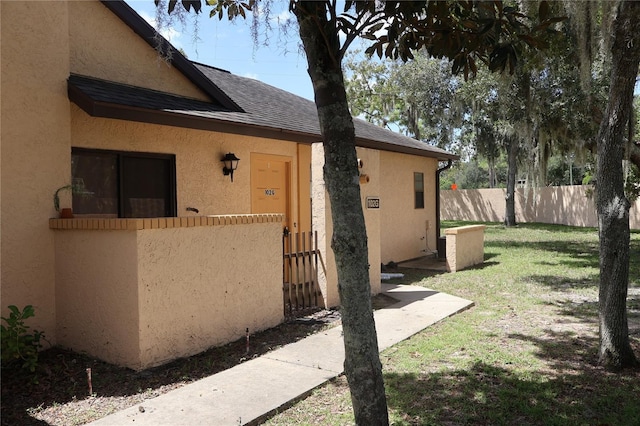 doorway to property featuring a yard, fence, a shingled roof, and stucco siding