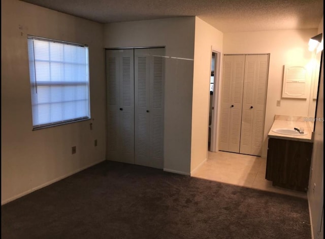 unfurnished bedroom with carpet floors, two closets, and a sink