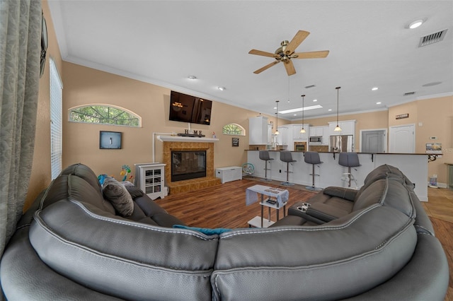 living area featuring crown molding, a ceiling fan, wood finished floors, and visible vents