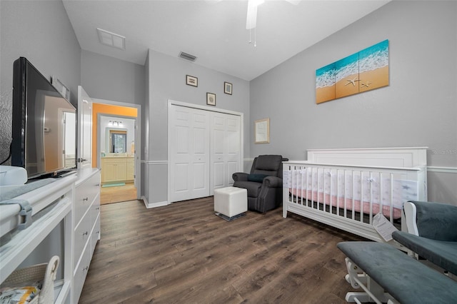 bedroom featuring a nursery area, dark wood finished floors, visible vents, and a closet