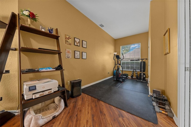 workout area featuring baseboards, vaulted ceiling, wood finished floors, and visible vents