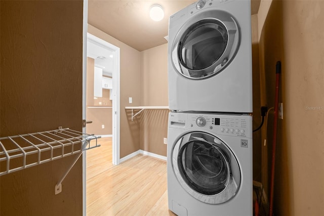 clothes washing area with baseboards, light wood-style floors, laundry area, and stacked washer / drying machine