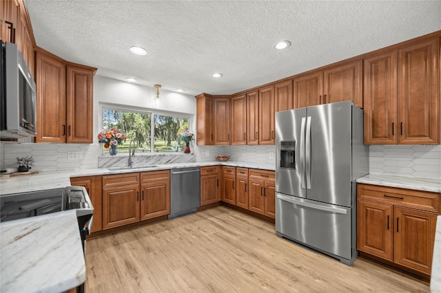 5326 NW 76th Ct, Ocala, FL 34482 - kitchen with stainless steel appliances, brown cabinetry, a sink, light wood-type flooring, and backsplash