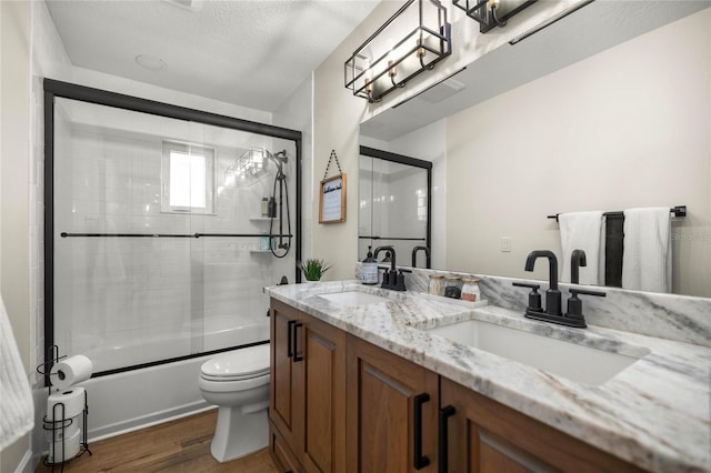 5326 NW 76th Ct, Ocala, FL 34482 - bathroom featuring wood finished floors, double vanity, shower / bath combination with glass door, toilet, and a textured ceiling