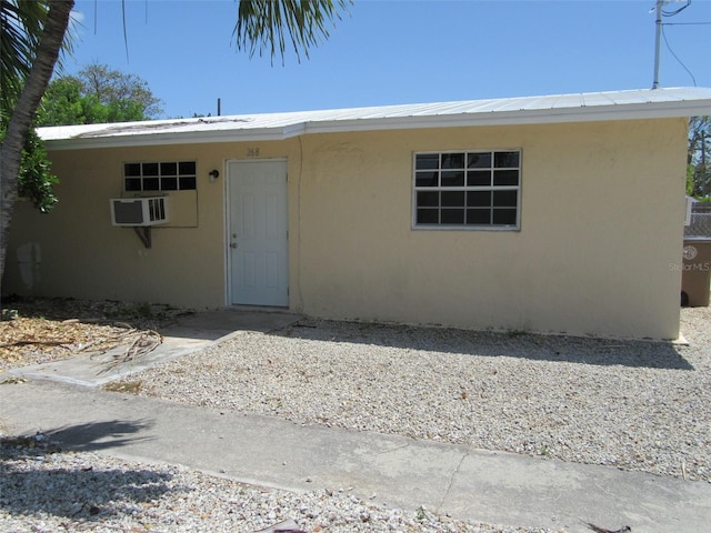 view of front facade with a wall mounted air conditioner and stucco siding