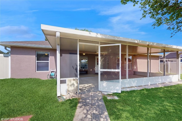 back of house featuring a lawn, stucco siding, and a sunroom