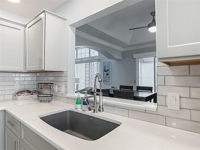 kitchen with a sink, crown molding, ceiling fan, backsplash, and light countertops