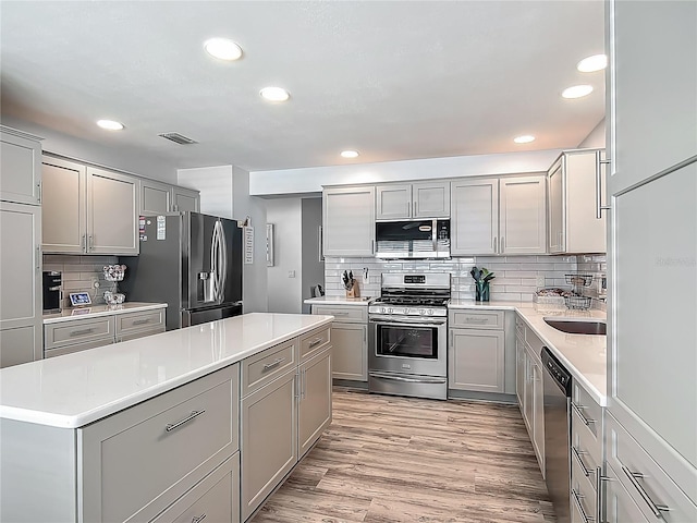 kitchen with gray cabinetry, light countertops, stainless steel appliances, and tasteful backsplash