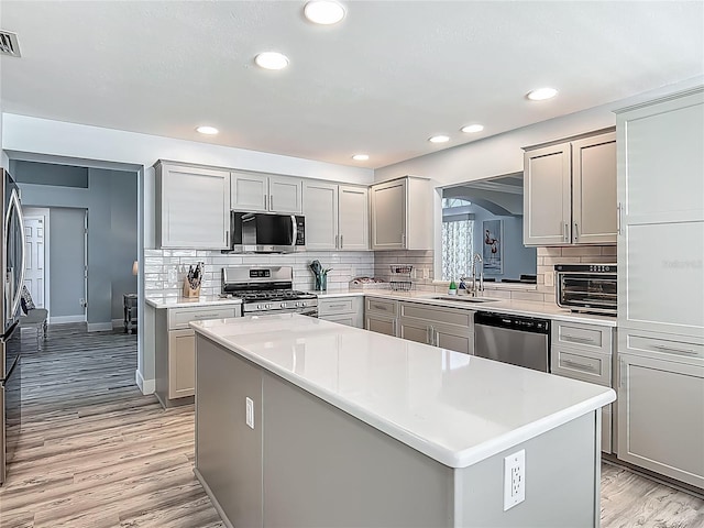 kitchen with decorative backsplash, appliances with stainless steel finishes, gray cabinetry, and a kitchen island