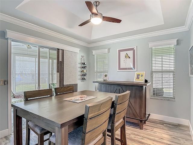 dining room featuring light wood finished floors, a ceiling fan, a tray ceiling, baseboards, and ornamental molding