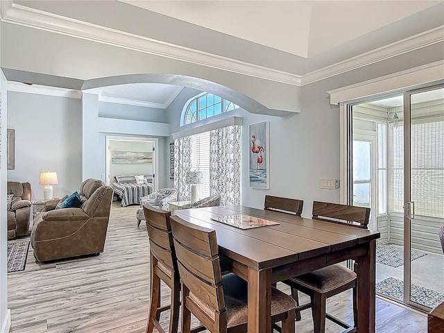 dining room featuring light wood finished floors, crown molding, and arched walkways