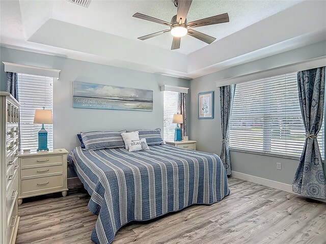 bedroom featuring a tray ceiling, ceiling fan, baseboards, and light wood-style floors