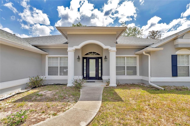 doorway to property featuring a lawn, roof with shingles, and stucco siding