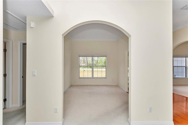 carpeted spare room with crown molding, arched walkways, and baseboards
