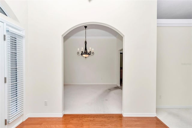 unfurnished dining area with baseboards, arched walkways, wood finished floors, and a chandelier