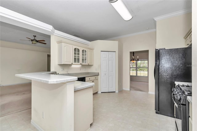 kitchen featuring cream cabinets, crown molding, range with gas stovetop, ceiling fan with notable chandelier, and a peninsula