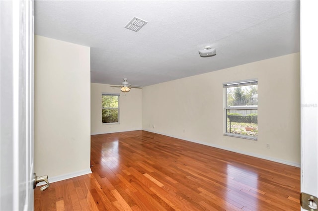 empty room with plenty of natural light, wood-type flooring, ceiling fan, and visible vents