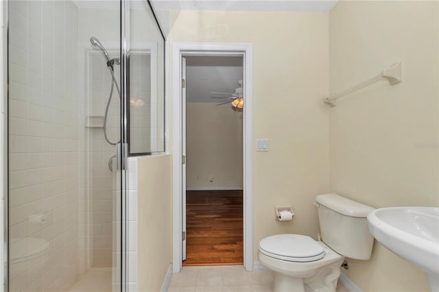 bathroom featuring toilet, baseboards, ceiling fan, a shower stall, and a sink