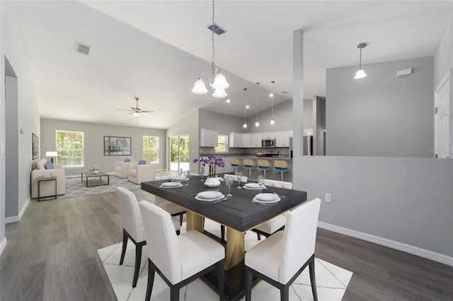 dining space with wood finished floors, vaulted ceiling, a ceiling fan, baseboards, and a chandelier