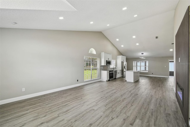 1317 Ravida Woods Dr, Apopka, FL 32703 - unfurnished living room featuring high vaulted ceiling, light wood-style flooring, recessed lighting, baseboards, and a sink