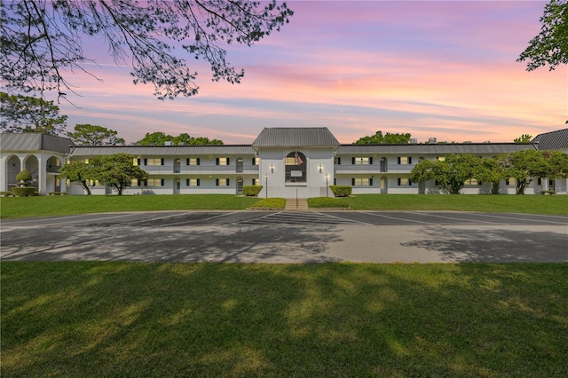 view of front facade with uncovered parking, metal roof, and a lawn