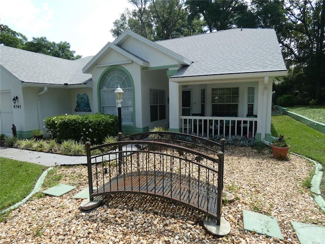 view of front of home with a porch, a shingled roof, stucco siding, and a front lawn