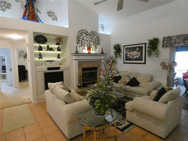 living area with light tile patterned floors, a glass covered fireplace, ceiling fan, and high vaulted ceiling