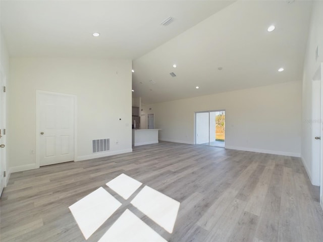 unfurnished living room featuring light wood finished floors, visible vents, baseboards, and high vaulted ceiling