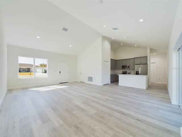 unfurnished living room with baseboards, light wood finished floors, visible vents, and high vaulted ceiling